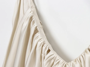 Close-up of pleated satin fabric detailing on an ivory elegant sleeveless top