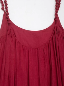 Détail d'une robe rouge à bretelles avec tissu texturé et finitions à petits pompons