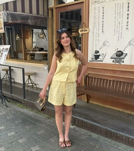 Detail of light yellow sleeveless buttoned top and high-waist linen shorts set