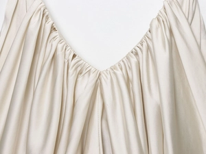 Detail of V-neckline featuring pleated silk satin fabric in champagne color