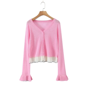 Detail of pink knit cardigan showing ruffled hem and flared cuffs with contrast stitching