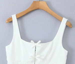 Detail of white camisole top featuring square neckline and delicate bow accents