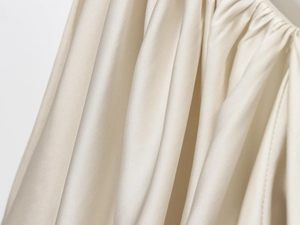 Detailed macro view of champagne satin fabric showing fine pleats and silky texture