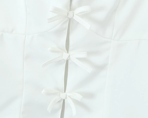 Detail of white camisole top featuring decorative 3D bow ties and delicate fabric texture