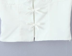 Detail of white top featuring delicate bow ties and fine fabric texture on violet background
