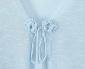 Close-up of light blue knitted cardigan with tie-up closure and crochet floral details