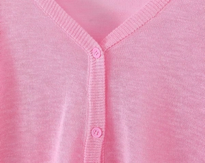 Detailed close-up of V-neckline with resin buttons on a soft pink ruffled knit cardigan