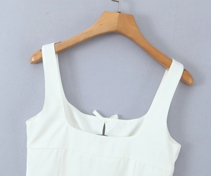 Detail of white square neck top with bow decoration on a wooden hanger