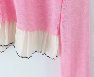 Detailed view of pink knitted top featuring white chiffon ruffle hem and black wavy edges