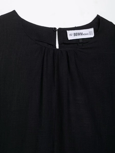 Détail de l'encolure du haut en lin avec des plis délicats et fermeture à bouton noir