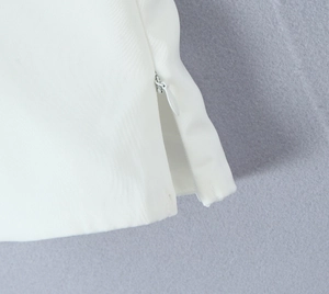Detail view of a white woven top featuring an invisible side zipper and a subtle slit design