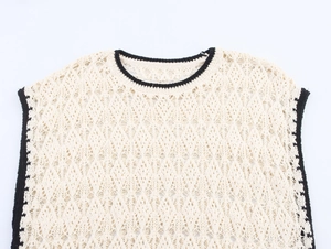 Dettaglio del gilet in maglia traforata con bordi neri a contrasto su tessuto bianco crema
