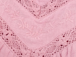 Detail of pink cotton fabric featuring leaf embroidery and V-shaped lace inserts