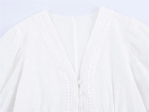 Detail of white eyelet embroidery lace fabric with V-neckline and fabric buttons