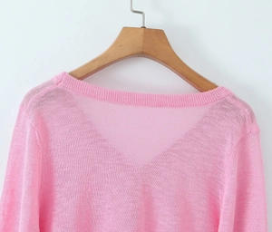Detail of pink knitted cardigan with mesh texture and ruffle trim on wooden hanger