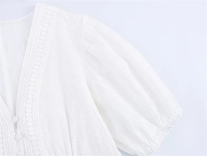 Close-up of white eyelet lace dress with V-neckline, puff sleeves and elegant button detail