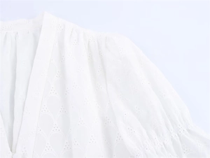 Macro detail of white eyelet embroidery on a V-neck dress with elegant pleated shoulders