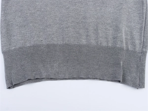 Detailed close-up of the grey knitted sweater's ribbed hem showing fabric texture
