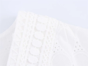 Detailed close-up of white cotton fabric with geometric embroidery and lace cutouts