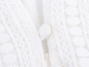 Macro detail of white lace dress showing intricate hollow embroidery and fabric button