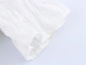 Detailed macro view of white eyelet embroidery and elastic smocked cuffs on the dress