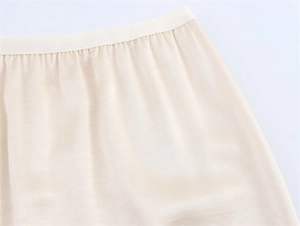 Detail of elegant pleated beige satin skirt featuring an elastic waistband and fine pleats