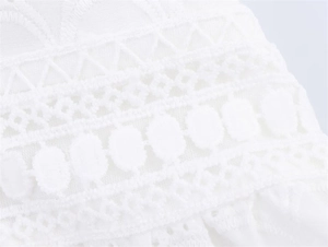 Detail of white embroidered fabric featuring intricate hollow lace and geometric patterns