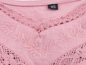 Close-up of pink cotton fabric with floral embroidery and lace V-neck detail