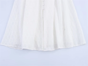 Close-up of white eyelet embroidery dress with central fabric-covered buttons detail