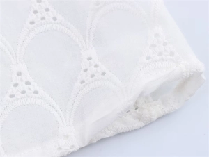 Close-up of white dress fabric with intricate embroidery and scallop hollow-out details