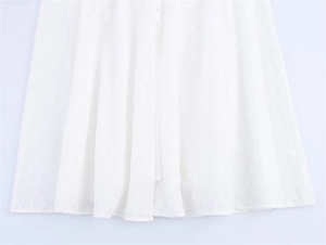 Close-up of white dress showing intricate broderie anglaise embroidery and fabric buttons