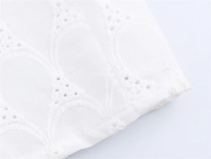 Detailed close-up of white dress fabric featuring elegant hollow wave embroidery patterns