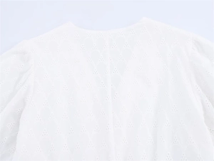 Close-up of white dress neckline with delicate broderie anglaise embroidery and pleated shoulders