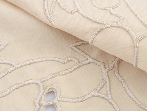 Detail of beige eyelet embroidery fabric with intricate floral patterns and refined textures