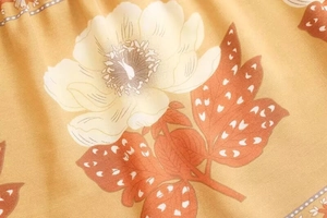 Detailed macro view of mustard yellow floral print fabric with white blossoms and red leaves