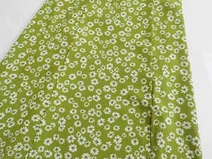 Close-up detail of green summer dress fabric with small white daisy floral print and side slit