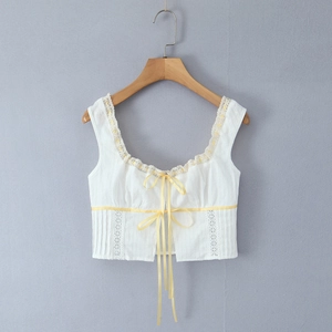 Detail of white cotton camisole with yellow ribbon bows and delicate floral lace trim