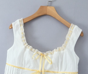 Detail of white sleeveless top showing beige lace trim and yellow ribbon bow accent