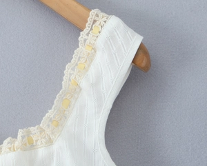 Detail of white sleeveless top showing lace trim, yellow ribbon, and floral texture