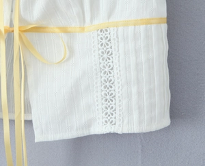 Detail of white eyelet embroidery fabric with yellow satin ribbon and floral lace insert