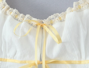 Detail of white top showing cross-jacquard texture with lace trim and yellow satin bow