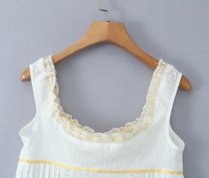 Detail of white sleeveless top with lace trim, yellow ribbon, and textured stripes