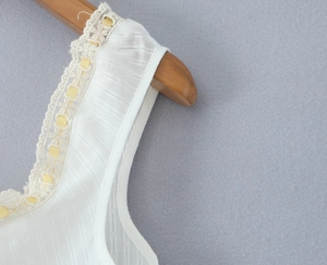 Detail of white dot texture fabric with lace trim and pale yellow ribbon on neckline
