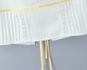 Detail of white pleated fabric with eyelet embroidery and contrast yellow ribbon trim
