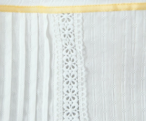 Detailed view of white fabric featuring floral lace stitching and yellow silk ribbon trim