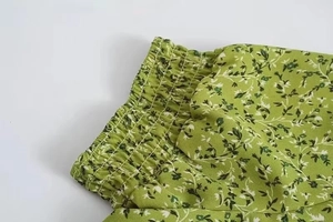 Detail of green floral dress featuring elastic smocked waist and delicate ruffle trim