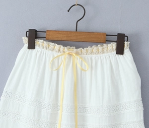 Close-up of white skirt detailing lace patchwork and a pale yellow satin ribbon bow