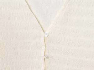 Détail d'une blouse crème à col en V avec tissu texturé et boutons blancs