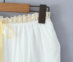 Detail of white jacquard skirt featuring cream lace trim and a yellow satin ribbon tie