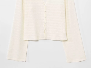 Vue détaillée de l'aspect texturé et des boutons sur le cardigan de couleur blanc cassé